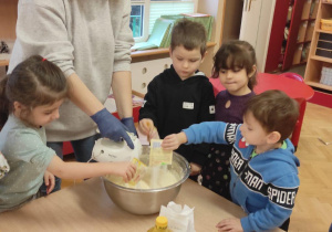 Dzieci razem z nauczycielką mieszają mikserem ciasto na pierniczki.