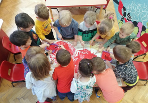 Dzieci wspólnie malują czerwoną farbą wielkie serce.