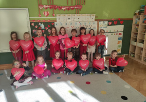 Ustawione dzieci, trzymają w dłoniach czerwony balon w kształcie serca.