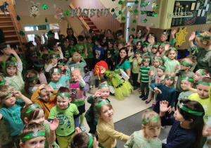 Symboliczna chwila topienia Marzanny. Dzieci ze wszystkich grup są ubrane na zielono i stoją na holu głównym. Nauczycielka topi Marzannę.