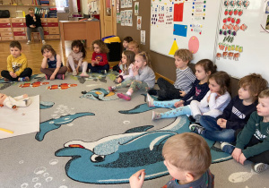 Dzieci siedzą na dywanie i patrzą na panią instruktor podczas warsztatów Labolo.