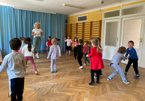 Dzieci tańczą w rozsypce przy muzyce razem z panią instruktor.