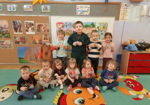 Dzieci stoją i siedzą pod tablicą i prezentują swoje medale Super Przedszkolaka.