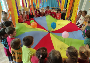 Zabawy chustą animacyjną. Dzieci stoją dookoła chusty animacyjnej i poruszają nią sprawiając, że balony się unoszą.