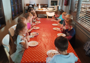 Dzieci siedzą przy stole i próbują wcześniej samodzielnie przygotowanych pierogów.