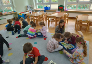 Dzieci siedzą na dywanie w małych grupkach i starają się zbudować własnego robota z klocków Lego na zajęciach z robotyki.