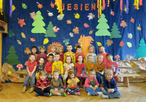 Dzieci pozują do zdjęcia grupowego na tle jesiennej dekoracji.