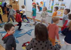 Dzieci poruszają się po dywanie w rytm muzyki lecącej z radia.