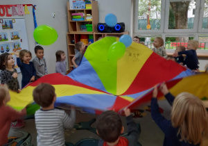 Dzieci poruszają chustą animacyjną i wprawiają balony w ruch, które unoszą się do góry.