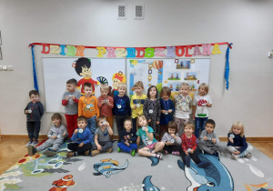 Dzieci siedzą oraz stoją na dywanie i prezentują medale Super Przedszkolaka.