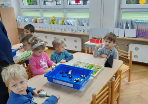 Dzieci siedzą przy stoliku i zapoznają się z klockami Lego.