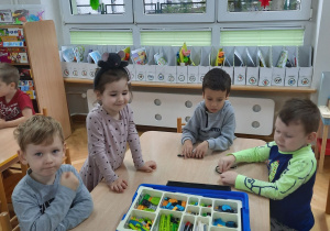 Trzech chłopców i dziewczynka siedzi przy stoliku i zapoznaje się z klockami Lego.