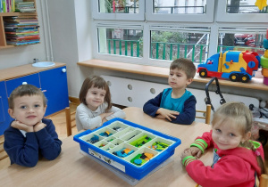 Dwie dziewczynki i dwóch chłopców siedzi przy stoliku i zapoznaje się z klockami Lego.