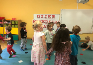 Dzieci ustawione w małych kółkach tańczą do piosenek dziecięcych.