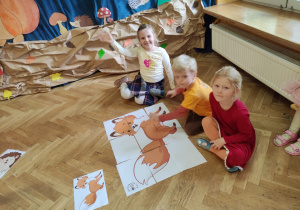 Dzieci siedzą na podłodze i prezentują ułożone giga puzzle z wizerunkiem liska.
