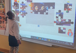 Dziewczynka wykonuje zadanie na tablicy multimedialnej - układa puzzle.