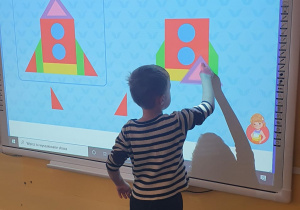 Chłopiec wykonuje zadanie na tablicy multimedialnej - buduje rakietę z figur geometrycznych.