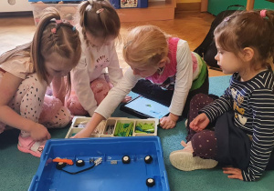 Dzieci siedzą na dywanie i układają robota z klocków Lego, a instrukcja wykonania wyświetla im się na tablecie.