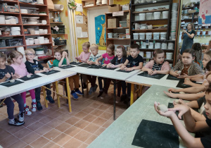 Dzieci siedzą przy stole i lepią z gliny.