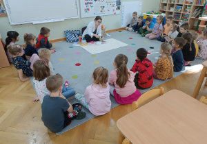 Dzieci siedzą w półkolu, a prowadząca wykonuje eksperyment napełniając tubkę kolorowymi koralikami.