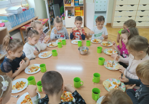 Dzieci siedzą przy stoliku i podczas drugiego śniadania jedzą sałatkę przez siebie przygotowaną.