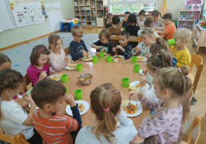 Dzieci siedzą przy stoliku i podczas drugiego śniadania jedzą sałatkę przez siebie przygotowaną.
