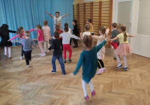 Dzieci wspólnie z trenerką zumby tańczą z rękami uniesionymi do góry.
