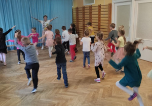 Dzieci wspólnie z trenerką zumby tańczą z rękami uniesionymi do góry.