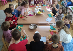 Dzieci siedzą przy stole jedzą przygotowane przez siebie "owocowe fantazje".