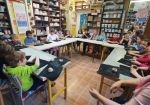 Dzieci siedzą przy dużym stole i lepią z gliny sówki w Pracowni Ceramicznej Amfora.