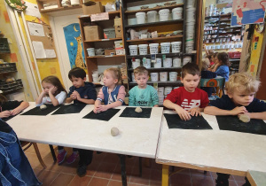 Dzieci siedzą przy dużym stole i lepią z gliny sówki w Pracowni Ceramicznej Amfora.