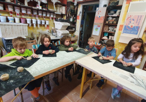 Dzieci siedzą przy dużym stole i lepią z gliny sówki w Pracowni Ceramicznej Amfora.