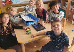 Dzieci siedzą przy stole i prezentują zrobionego przez nich robota z klocków lego.