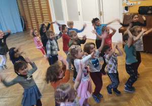 Dzieci z uniesionymi rączkami tańczą do szybkiej i rytmicznej muzyki.