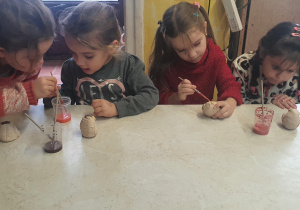 Dziewczynki siedzą przy dużym stole i malują sowy z gliny.