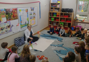 Dzieci siedzą w półkolu na dywanie i słuchają opowiadania o wielkim uczonym Archimedesie.