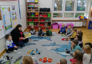 Akcja "Czytamy - głowy otwieramy". Dzieci siedzą w półkolu i uważnie słuchają czytanego im opowiadania przez jedną z mam.