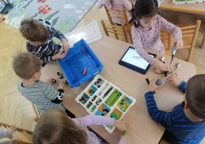 Dzieci siedzą przy stoliku i próbują zbudować robota z klocków Lego na zajęciach z robotyki.