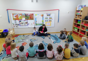 Akcja "Czytamy - głowy otwieramy". Dzieci siedzą w półkolu i słuchają opowiadania, które czyta im mama ich kolegi.