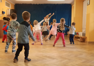 Dzieci uczą się nowych elementów układu tanecznego powtarzając ruchy za trenerką zumby.