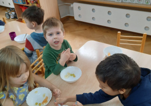 Dzieci nabierają łyżeczką pokrojone owoce i przekładają je do swoich miseczek.