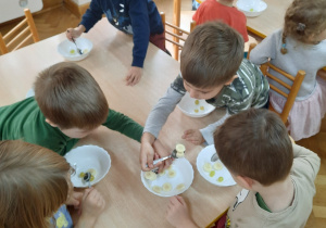 Dzieci nabierają łyżeczką pokrojone banany i przekładają je do swoich miseczek.