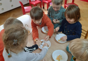 Dzieci nabierają łyżeczką pokrojone owoce i przekładają je do swoich miseczek.