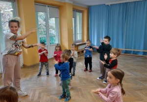Dzieci wspólnie z trenerką zumby tańczą do piosenki "Baby shark" z pokazywaniem.