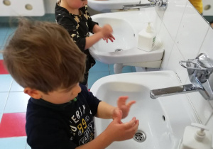 Chłopcy i dziewczynka próbują samodzielnie umyć rączki w łazience.
