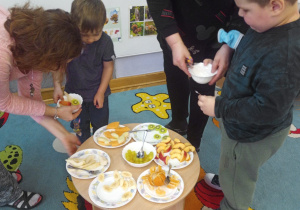 Dzieci z pomocą Pań nakładają sobie owoce do miseczek.