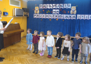 Dzieci stoją w rzędzie i czekają na uroczyste pasowanie przedszkolnym ołówkiem na przedszkolaka.