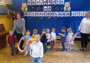 Dzieci stoją na środku sali wraz ze swoimi Paniami uśmiechają się i pozują do zdjęcia.