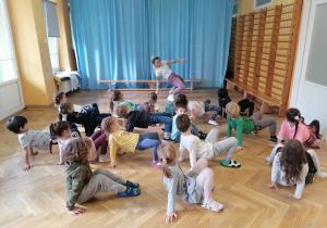 Dzieci siedzą na podłodze z rączkami opartymi za plecami i próbują się podnieść.