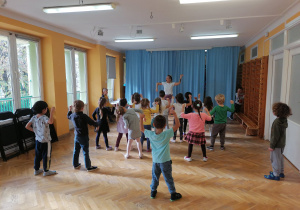 Dzieci stoją w rozsypance na sali i powtarzają układ taneczny za trenerką zumby.